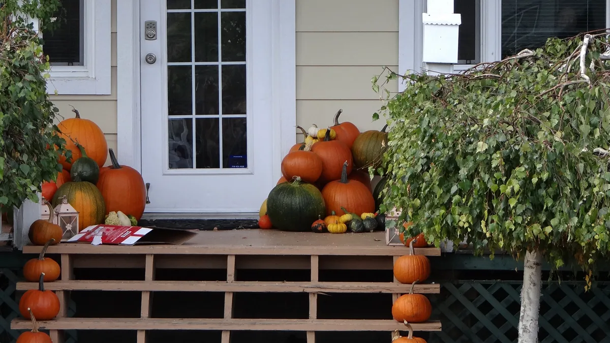 Residential front porch decorated with orange pumpkins and colorful fallen leaves in autumn