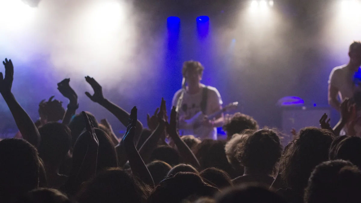 Concert fans standing at the front row barricade holding hands up toward the stage
