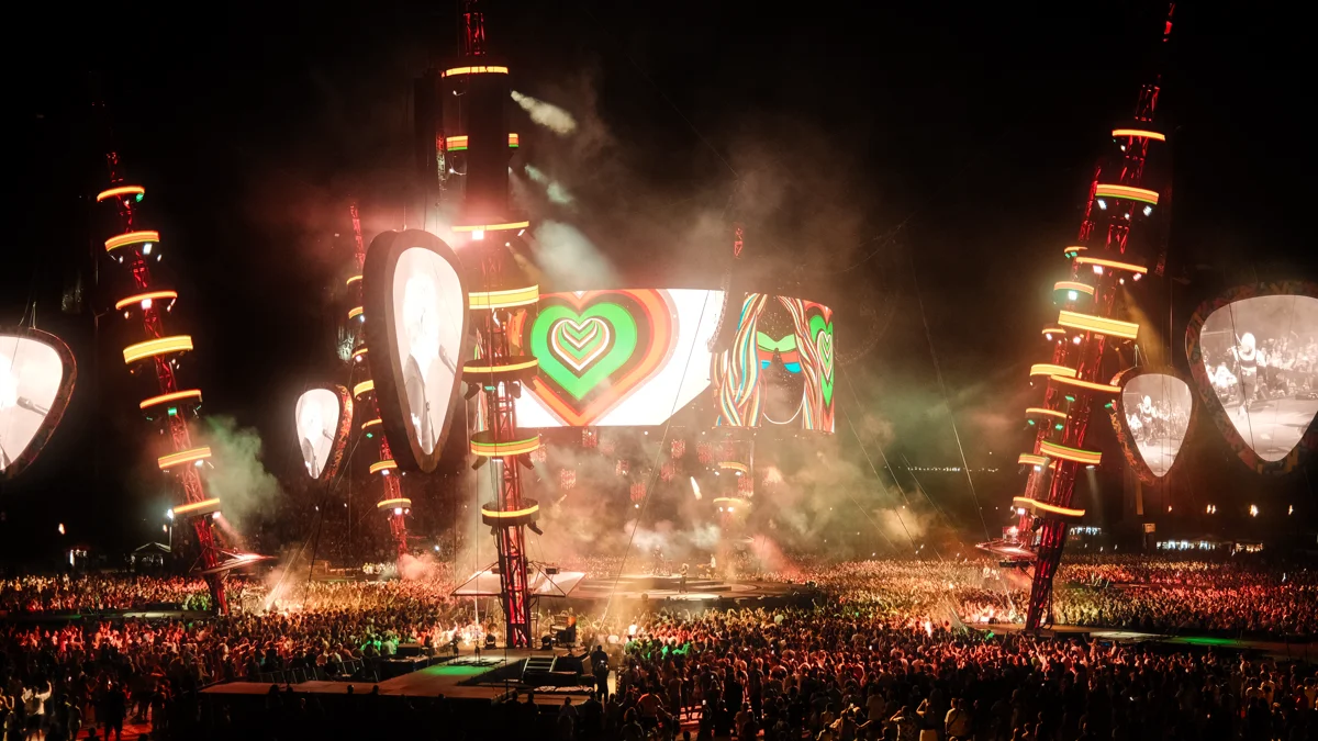 Audience watching a live outdoor stadium concert with bright stage illumination and colorful visuals